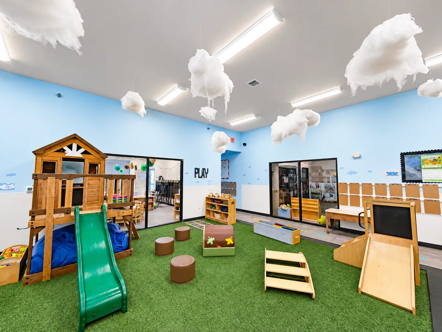 Indoor playground with wooden climbing house, green slide, and turf floor