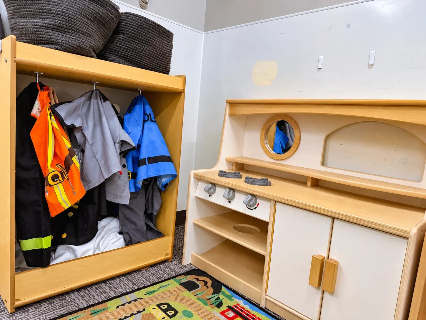 Dress-up closet with play clothes next to a wooden play kitchen
